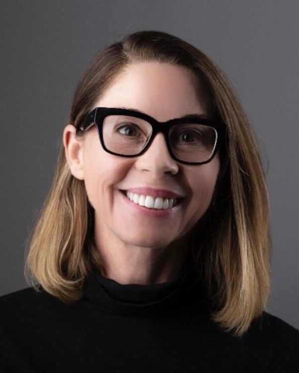 Eddie Lloyd is wearing thick glasses and a black turtleneck sweater, she is smiling.