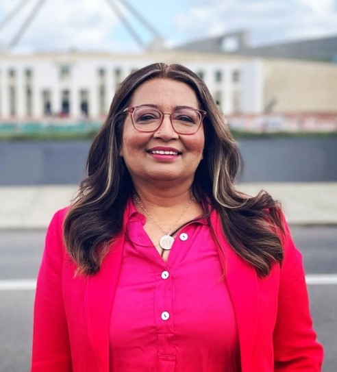 Mehreen is wearing a bright pink outfit and standing outside Parliament House in Canberra, she is smiling.